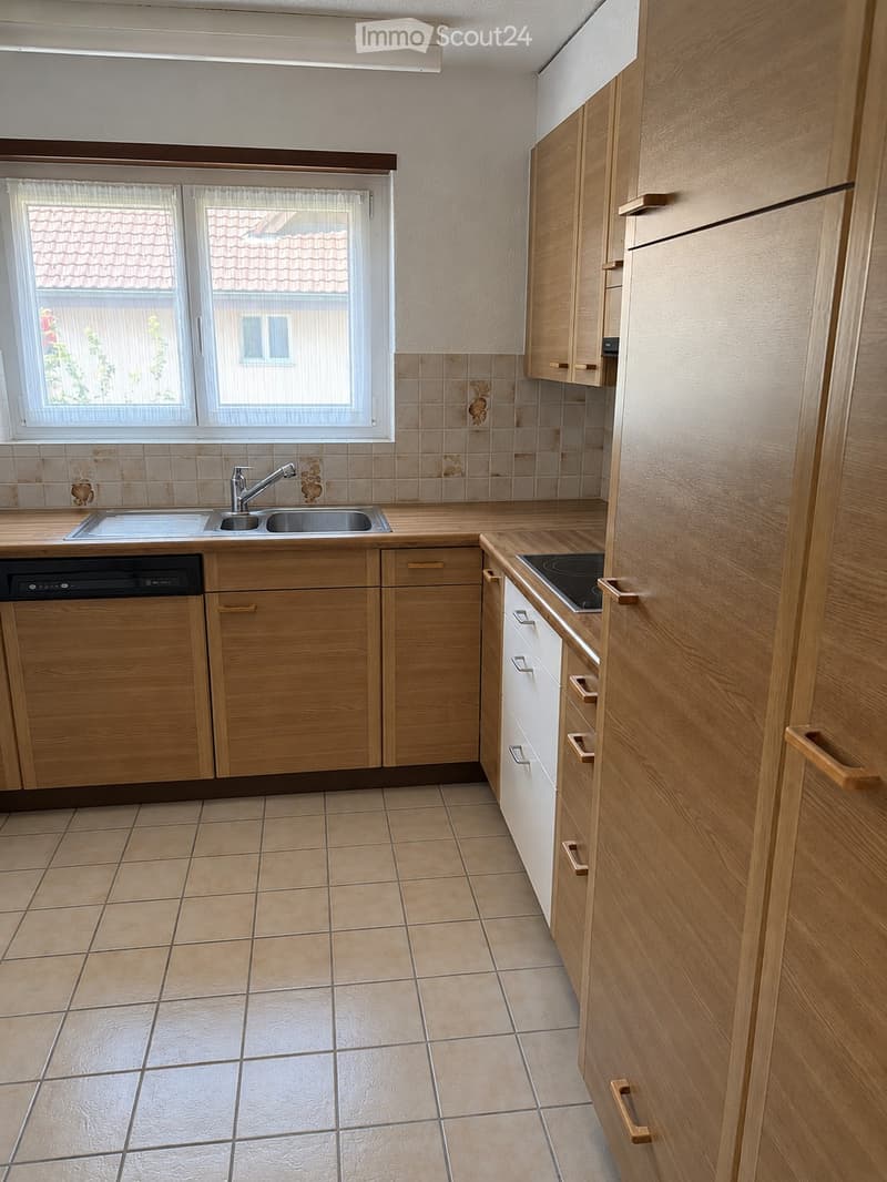 Modern kitchen with light wooden cabinets, tiled floor, and stainless steel sink and dishwasher.