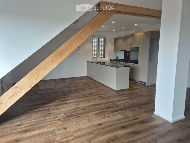 Open-plan kitchen and living area with wooden flooring, white kitchen island, modern cabinets, and a staircase leading to an upper level.