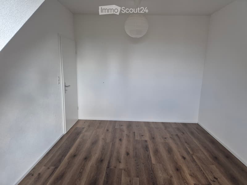 Empty room with wooden flooring and white walls, featuring a single door and a hanging light fixture.