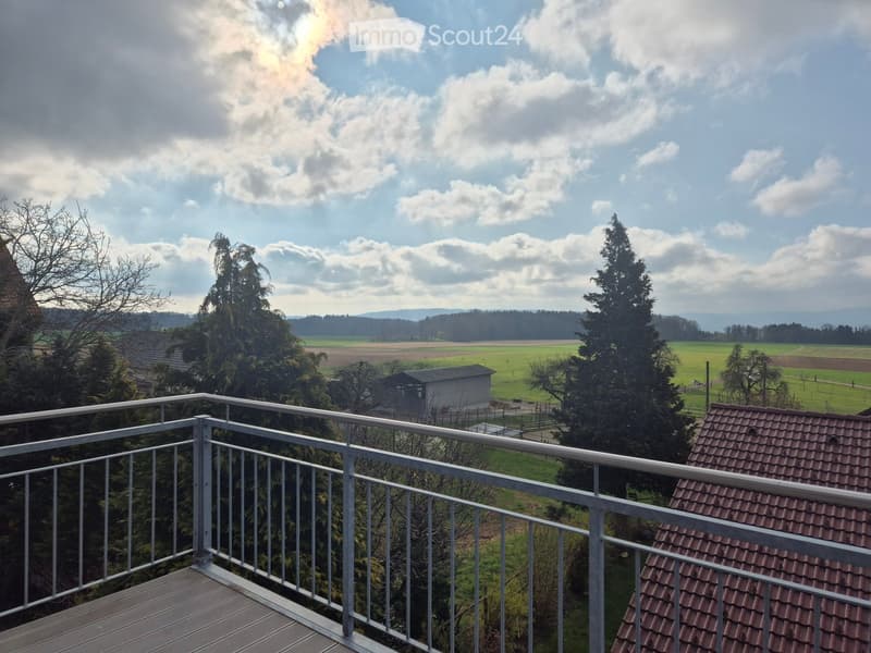 Balcony with metal railing overlooking a rural landscape with fields, trees, and a small building.