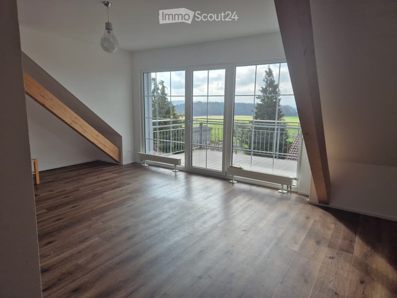 Empty room with wooden flooring, large windows, and a staircase leading upwards.