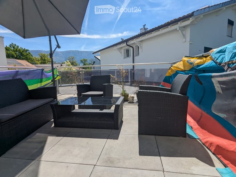 Outdoor terrace with a glass railing, wicker furniture, a glass coffee table, and a colorful canopy.