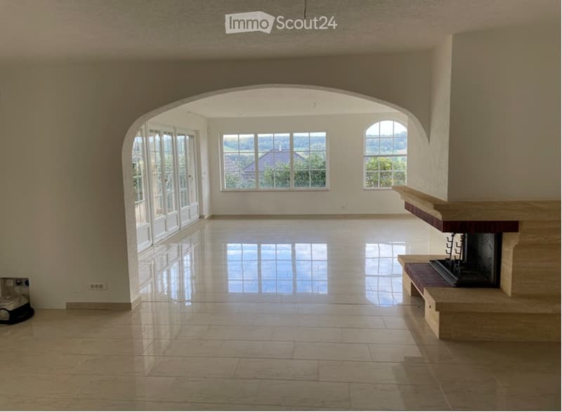 Empty living room with large windows, polished tile floor, and a fireplace. No furniture or equipment present.