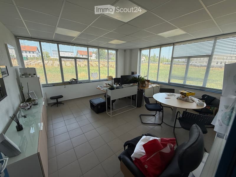 Office space with large windows, tiled floor, and modern furniture including desks, chairs, a laptop, and a plant.