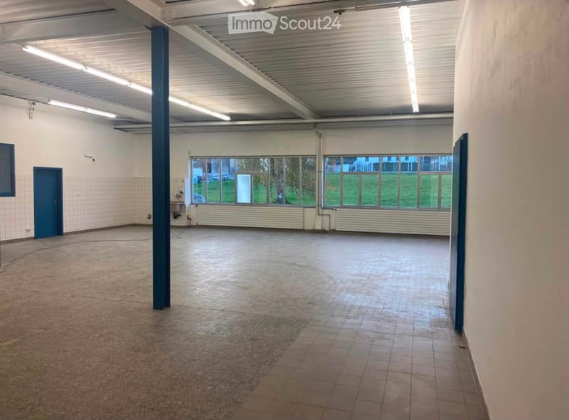 Empty room with bare walls, tiled and concrete floors, large windows, and a blue door.