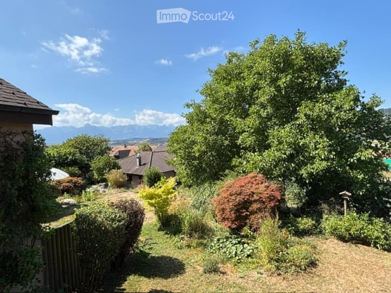 Well-maintained garden with various trees, shrubs, and a clear view of the surrounding landscape and mountains.