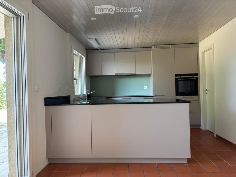 Modern kitchen with light-colored cabinets, a central island, and built-in appliances including an oven and sink.