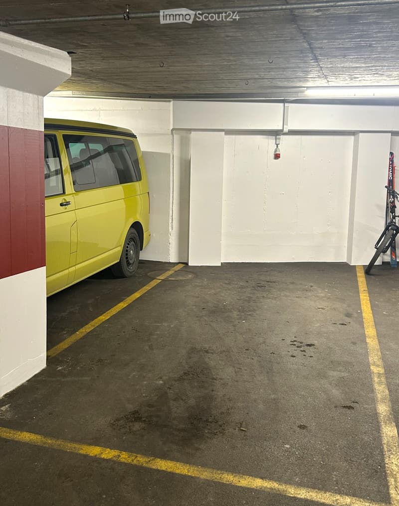 Yellow car parked, walls and ceiling are white and red, yellow parking lines, bicycle against the wall