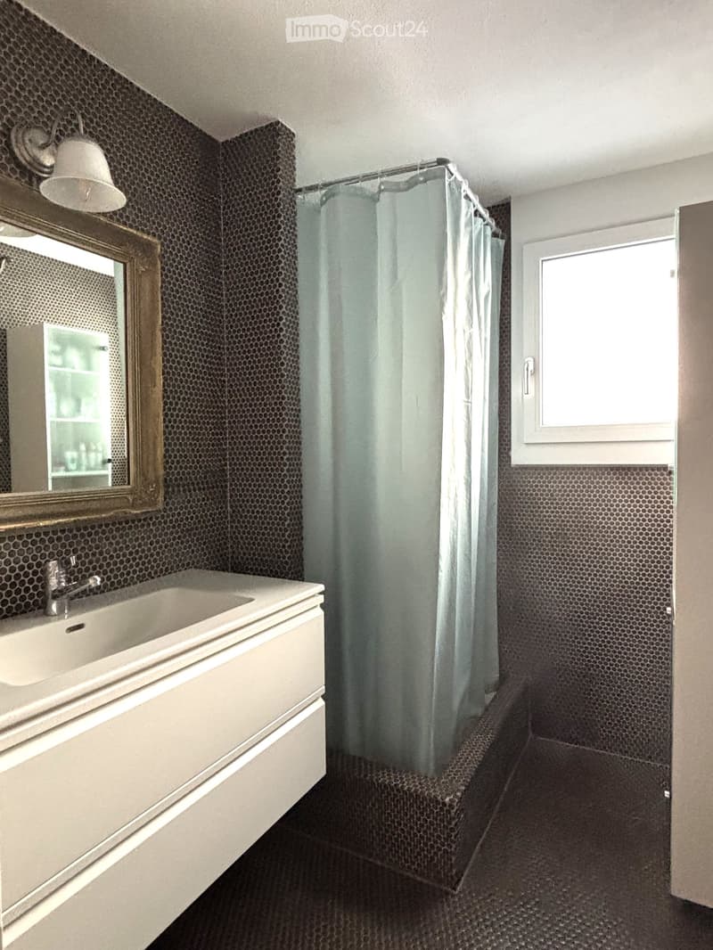 Bathroom with black tiled walls, white sink, shower curtain, mirror, and a window