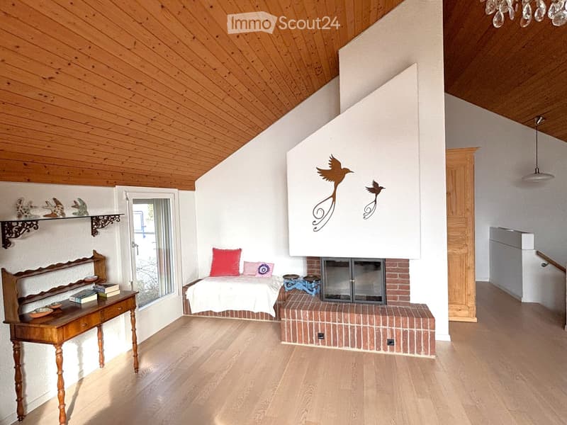 wooden ceiling, brick fireplace, white walls, bed with pillows, wooden desk, books on shelf, decorative items