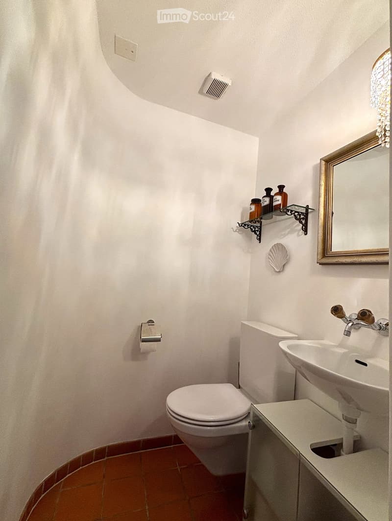 White toilet, white sink, white tiles, white toilet paper holder, gold mirror with a shell decoration.