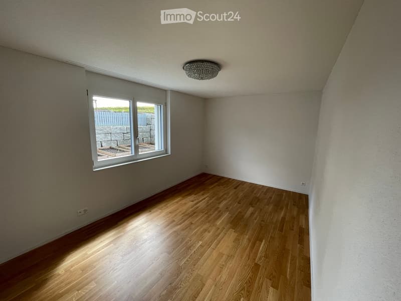 Empty room with wooden flooring, white walls, and a large window with a view of an outdoor area.