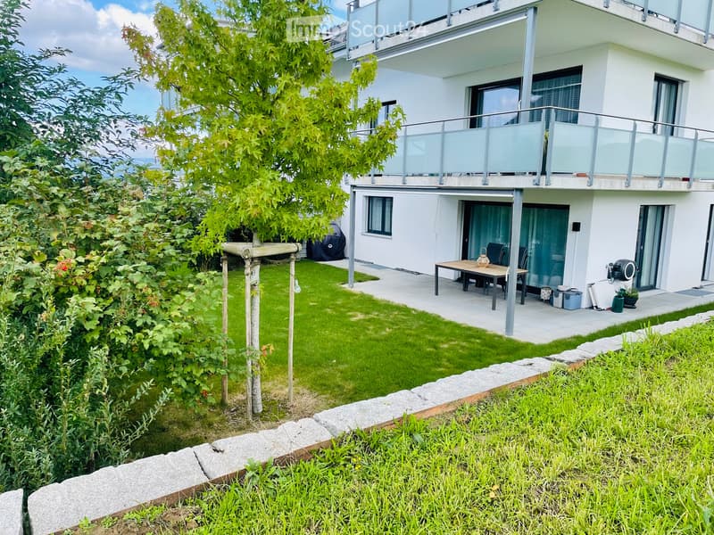 Modern two-story house with a well-maintained garden, patio furniture, and a balcony on the upper level.