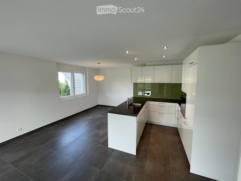 Modern kitchen with white cabinets, dark countertops, and a large window. Features a central island with a sink and built-in storage.