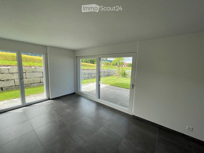 Empty room with large sliding glass doors leading to a patio and garden, tiled floor, and light-colored walls.