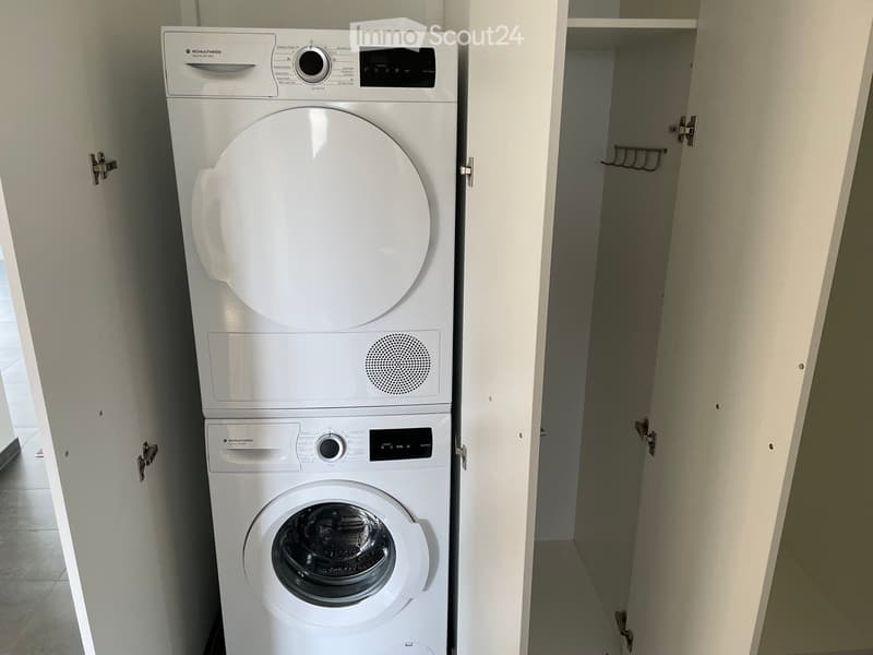 A compact bathroom with a stacked washing machine and dryer unit, white cabinetry, and a small shelf area.