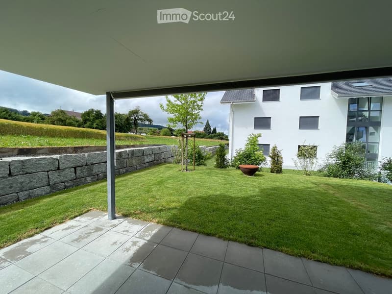 Well-maintained garden with a stone wall, green lawn, and a modern house in the background.