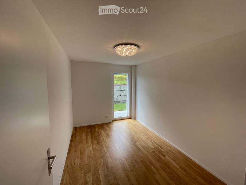 Empty room with wooden flooring, light-colored walls, and a ceiling light fixture. A sliding glass door leads to an outdoor area.