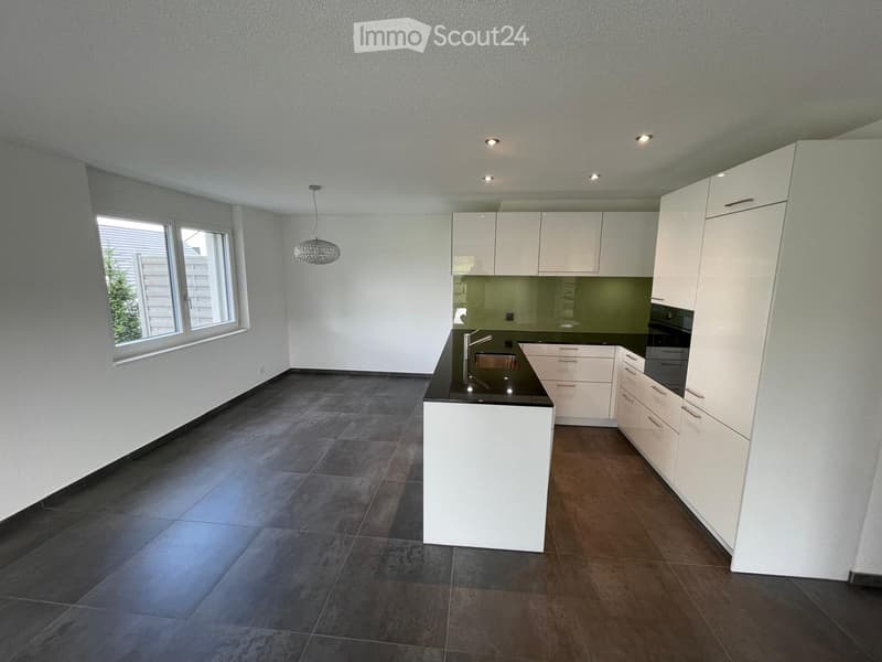 Modern kitchen with white cabinets, dark countertops, and stainless steel appliances. Features a large window and pendant lighting.