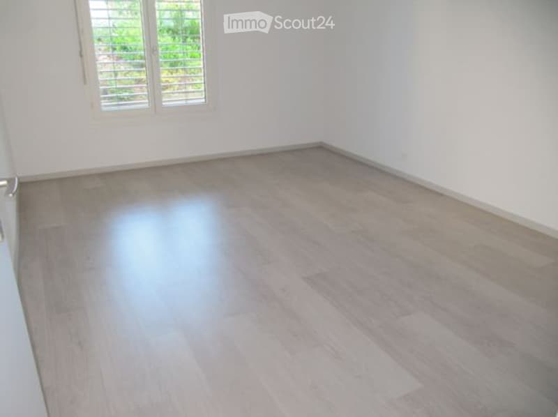 Empty room with light wooden flooring and white walls, featuring a single window with blinds.