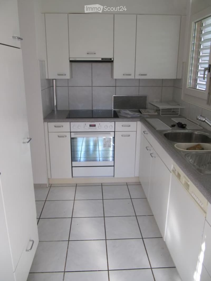 Modern kitchen with white cabinets, tiled floor, built-in oven, countertop, sink, and faucet.
