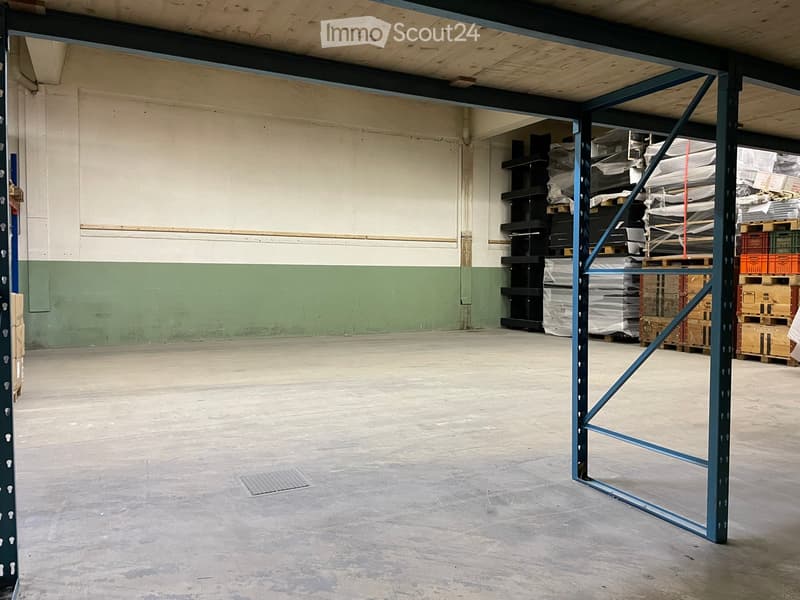 Empty warehouse space with concrete floor, metal shelving units, and stacked boxes in the background.
