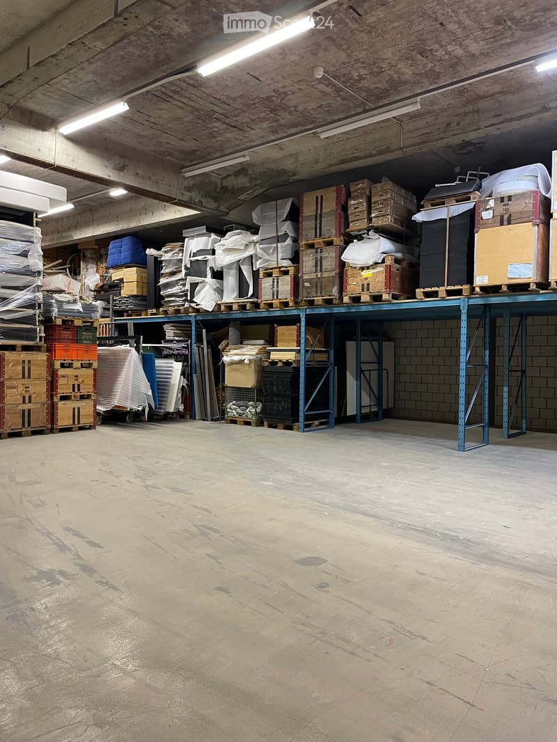 Warehouse space with concrete floors, metal shelving units, and various storage items including pallets, cardboard boxes, and containers.