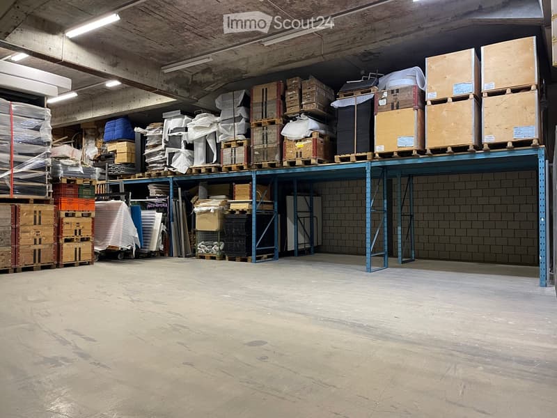 Warehouse space with concrete floor, metal shelving units, and stacked pallets and boxes.