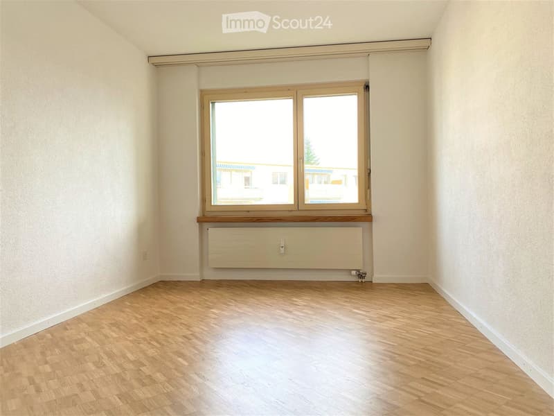 Empty room with light wooden flooring, white walls, and a large window with a radiator below it.