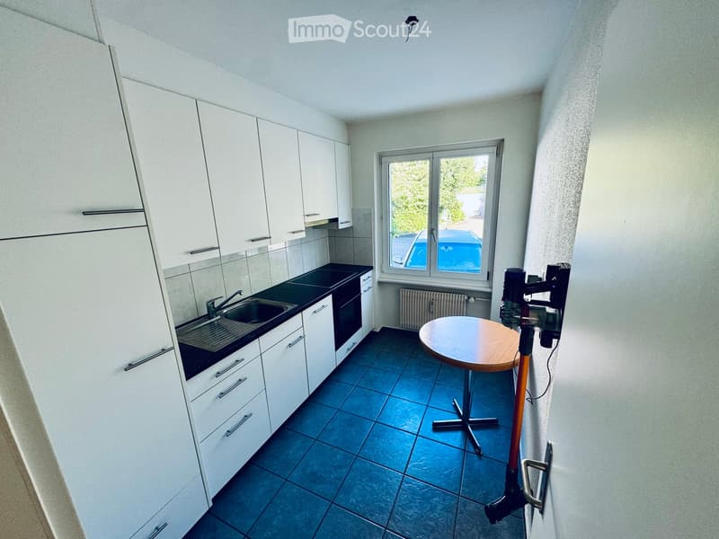 Modern kitchen with white cabinets, blue tiled floor, sink, and a small round table.