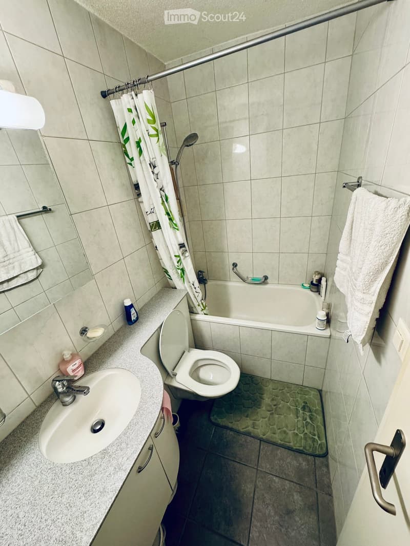 A compact bathroom with a white sink, toilet, bathtub, and shower curtain. The walls are tiled, and towels are placed on the side.