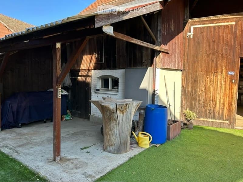 Outdoor area with artificial grass, wooden structure, tree stump table, blue barrel, covered furniture, and garden tools.