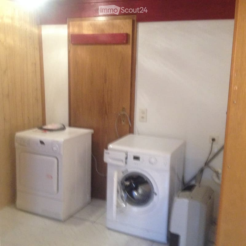 A small room with a washing machine and a dryer placed side by side, wooden door in the background.