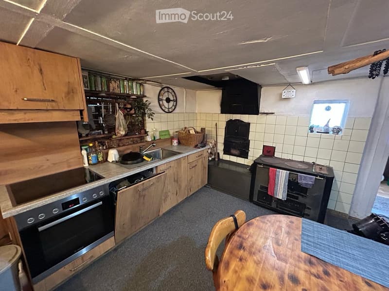 The kitchen features wooden cabinets, a stainless steel oven, a sink with a faucet, a wooden dining table with a chair, and a tiled backsplash.