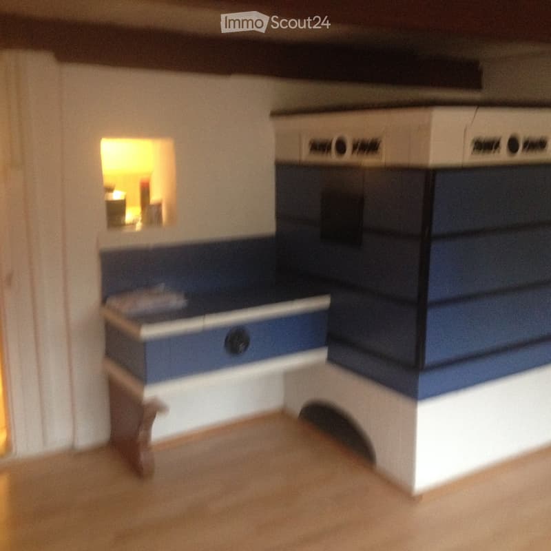 Empty room with a blue and white cabinet, wooden floor, and a small window showing a lit room beyond.