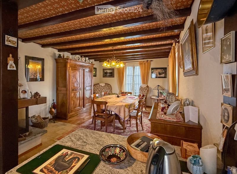 A cozy, rustic dining area with wooden furniture, a chandelier, and a fireplace. The room features a dining table with chairs, a large wooden cabinet, and various decorative items.