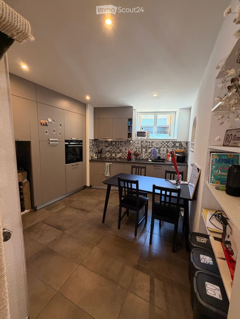 Modern kitchen with grey cabinets, tiled backsplash, and a dining area featuring a black table and chairs.