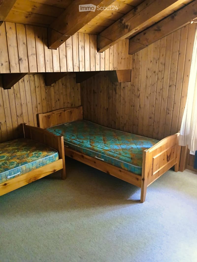 Cozy attic bedroom with wooden walls and slanted ceilings, featuring two single beds with colorful bedding.