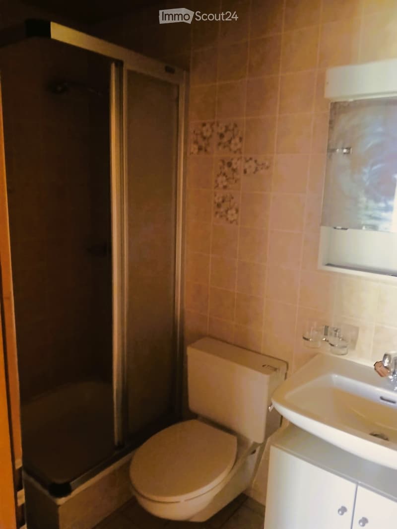 Bathroom with beige tiled walls, a toilet, a sink with a mirror above it, and a glass-enclosed shower area.