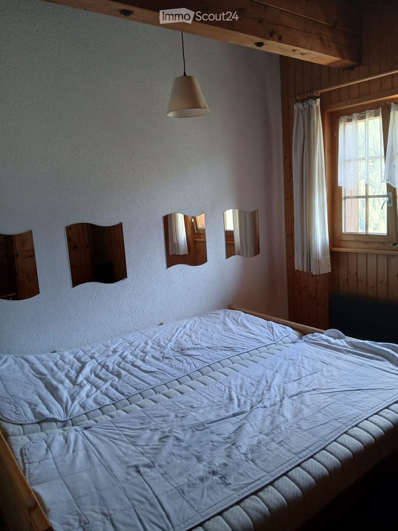 Cozy bedroom with a wooden bed frame, white quilted bedspread, three wall-mounted mirrors, a hanging pendant light, and a window with white curtains.