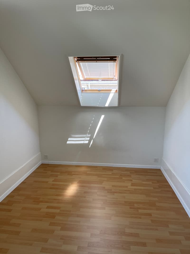 Empty room with wooden flooring, white walls, and a skylight window with blinds.