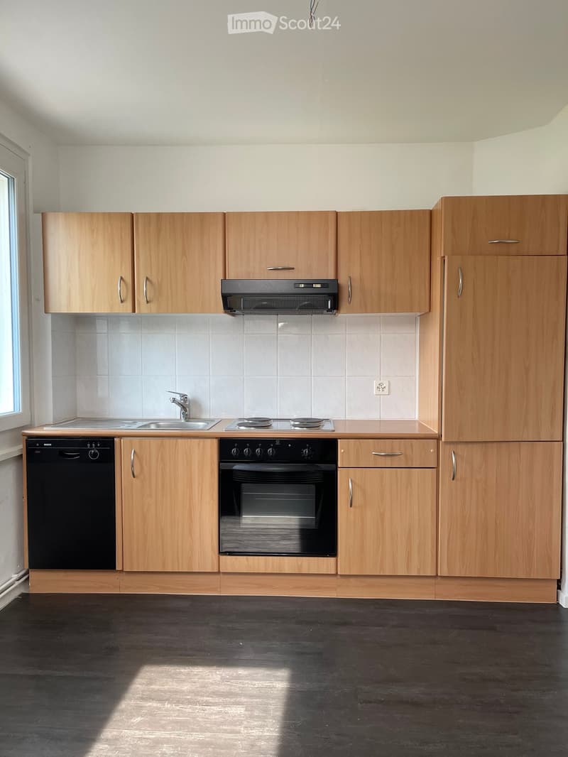 Modern kitchen with light wooden cabinets, stainless steel appliances, and a dark wooden floor.