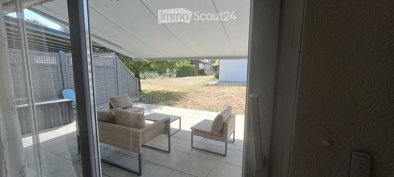 A covered patio with wicker furniture, including a sofa, chairs, and a small table, overlooking a grassy yard.