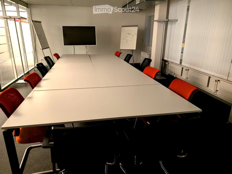Conference room with a long white table, red and black chairs, a large screen, and a whiteboard.