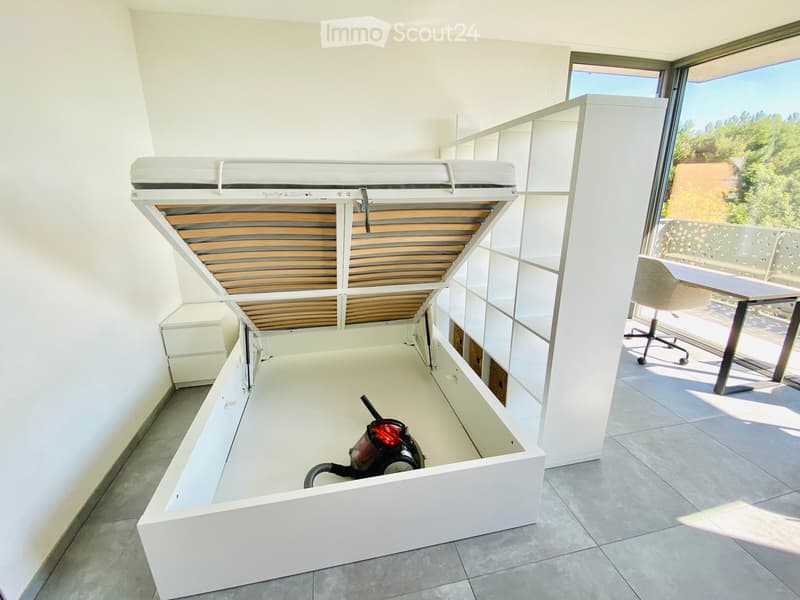An unfurnished room with a built-in bed system, white walls, tiled floor, and large windows offering a scenic view.