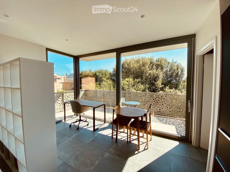 Modern balcony area with tiled floor, large glass doors, and outdoor furniture including a table and chairs.