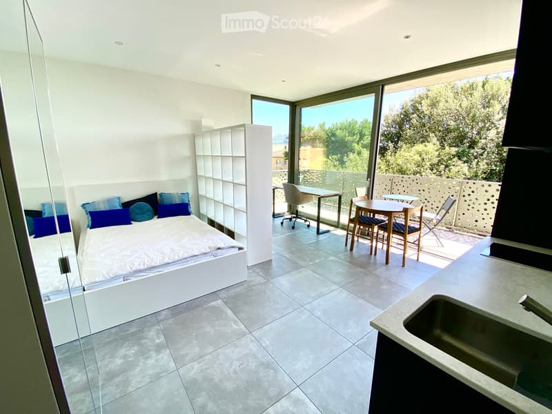 Modern, minimalist bedroom with a bed, shelves, and a small balcony area with a table and chairs.