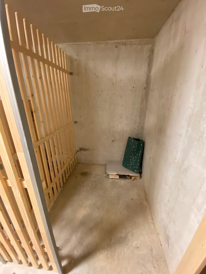Empty room with unfinished concrete walls and floor, wooden barrier on one side, and a small green bag on the floor.