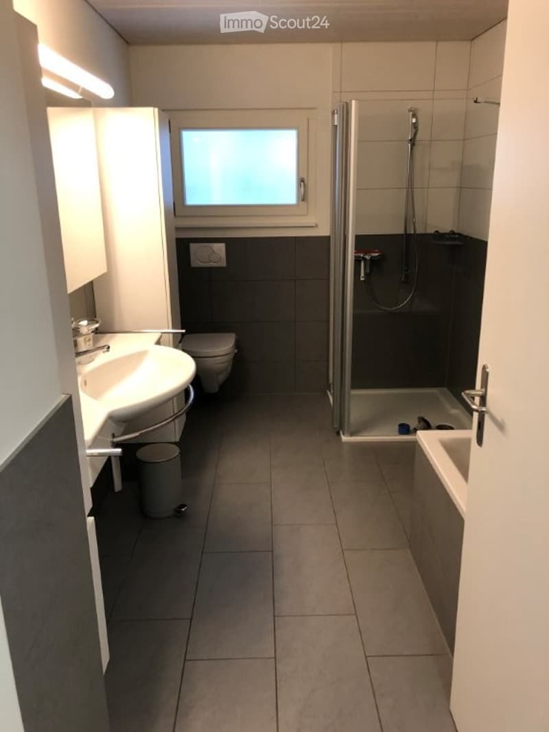Modern bathroom with a double sink, toilet, shower, bathtub, and a large window providing natural light. The space features tiled walls and floors, with a sleek, contemporary design.