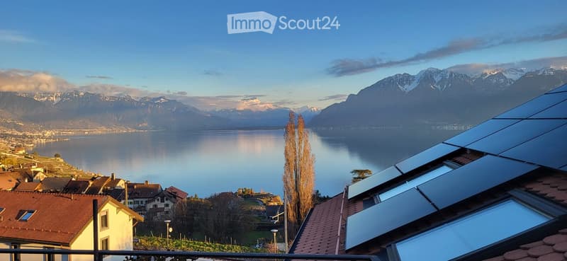 Panoramic view of a lake and snow-capped mountains from a rooftop with solar panels.